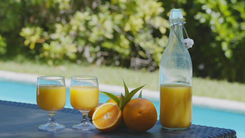 Freshly squeezed orange juice in a bottle and glasses stand on a table near the pool, a woman