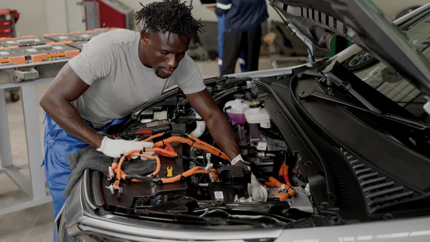 Professional African black male worker working service maintenance EV car in EV garage auto workshop, Cabling DC Inverter power line.