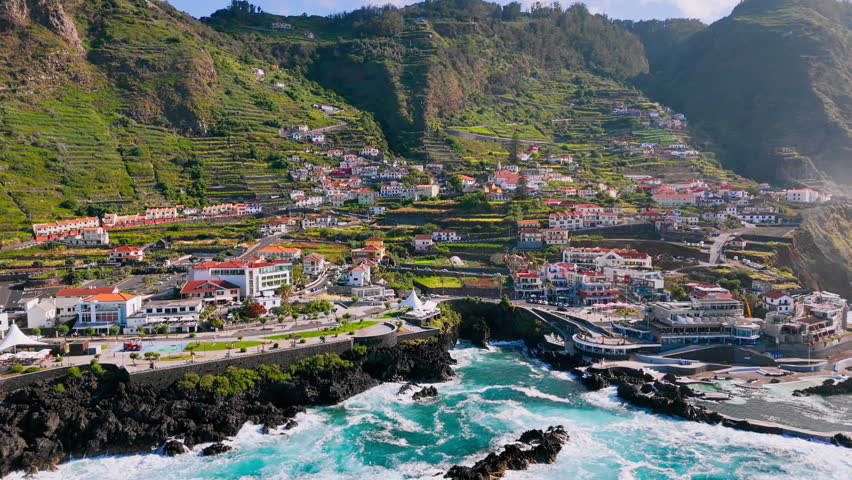 Aerial shot of Porto Moniz village and rugged Atlantic coastline with intense waves and clear sunlight on Madeira Island