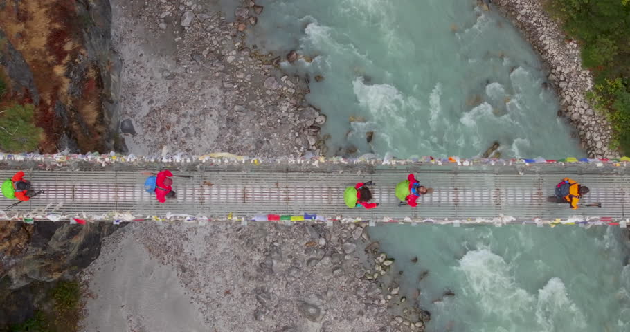 Everest region Nepal, top-down drone aerial shot of trekkers walking across the iconic Hillary Suspension Bridge above the rushing glacial waters of the Dudhkoshi River.