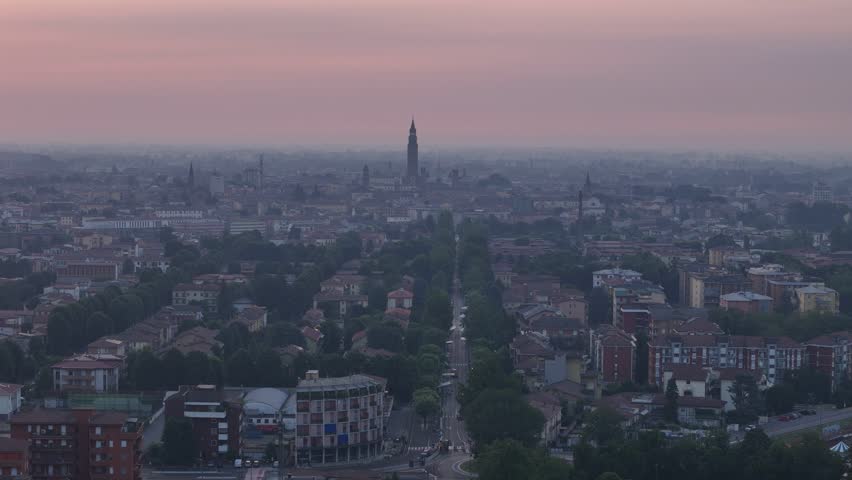 Golden sunrise illuminates the historic skyline of Cremona, featuring the Torrazzo, Cathedral and tree-lined Viale Po stretching toward the city center in Po Valley, Cremona, Lombardy, Italy. Aerial