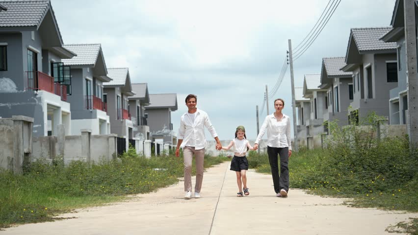 Happy family with father mother and daughter holding hand while walking together outside a new real estate residential housing property development neighborhood