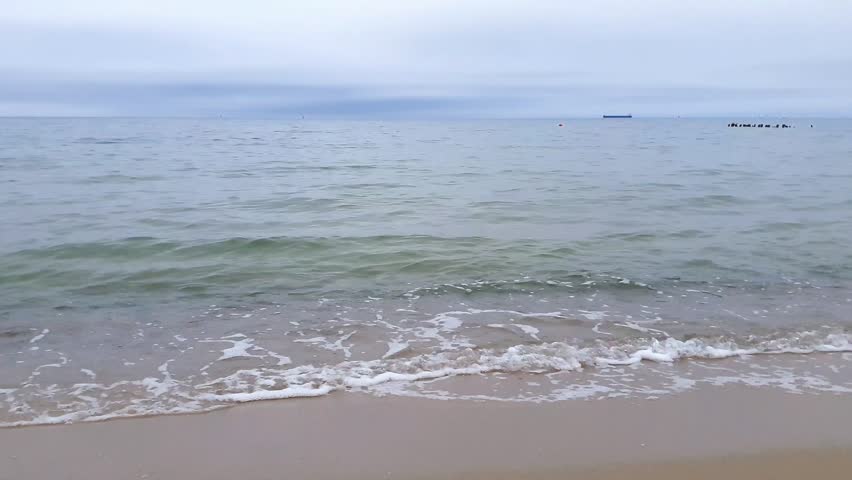 Serene seaside landscape with clean turquoise coastal surf water waves rolling on empty sand beach on Baltic sea shore under cloudy sky at overcast spring day. No people seascape natural background.