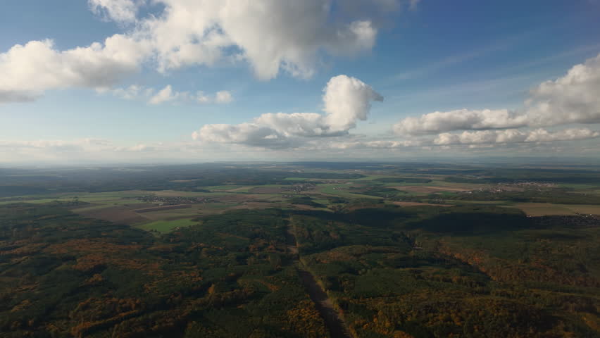 Flying under cumulus clouds over green canopy of forests and meadows on approaching Prague, natural scene from bird