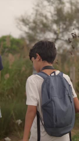 Young boy wearing a blue backpack hiking with his family through a field of tall grass, exploring a nature trail on an overcast day during a memorable outdoor summer adventure