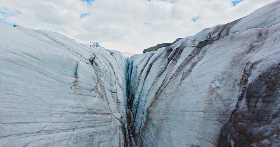 Dynamic FPV drone flight skimming above and between deep glacier crevasses on Vatnajökull Glacier, Iceland. Cinematic aerial footage revealing blue ice formations and dramatic glacial landscape.