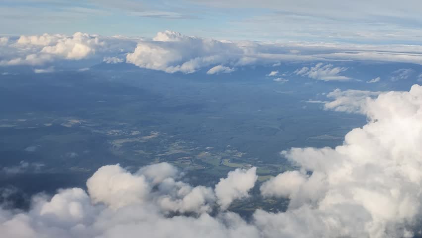 High altitude aerial footage of white cumulus clouds drifting over a landscape of green forests and fields in Washington state.