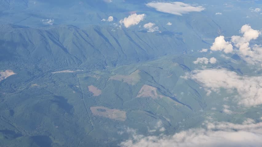 High altitude aerial footage of a vast mountain range covered in green forests with scattered white clouds drifting over the landscape in Washington state.