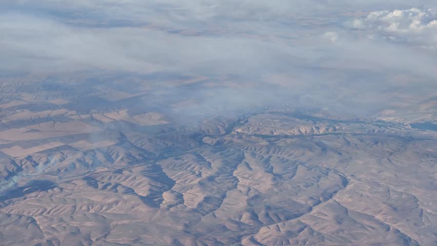 High altitude aerial footage of a dry, rugged landscape with rolling hills and valleys in Washington state, partially obscured by low-lying clouds.