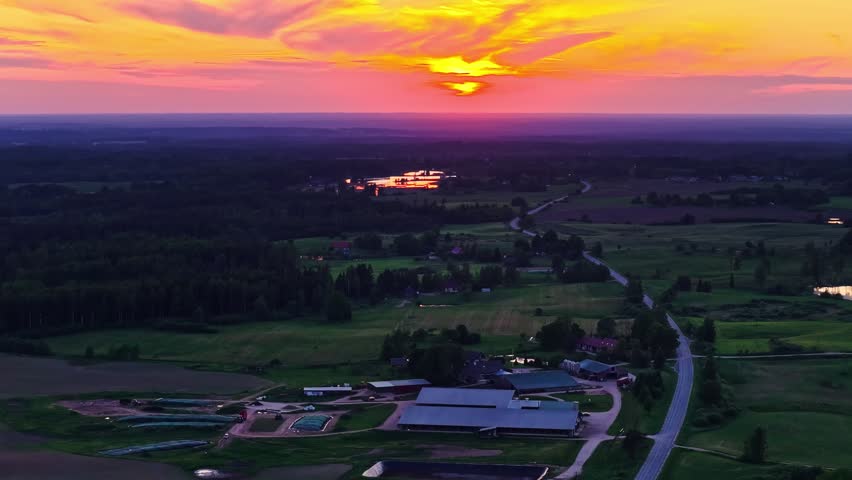 Aerial countryside at glowing sunset above farms, ponds and winding roads, drone panoramic pullback