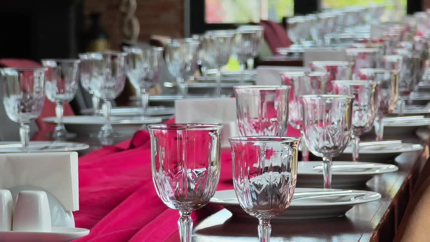 Beautifully decorated long table with crystal glasses, white plates, and red napkins prepared for a festive banquet or wedding reception
