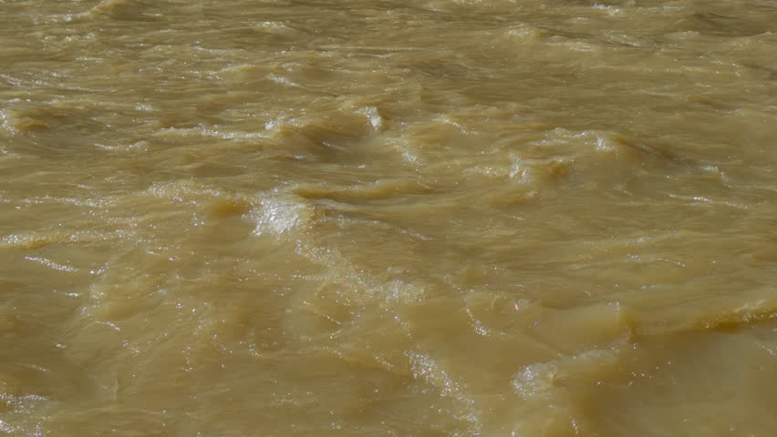 Closeup of muddy river water with flowing currents and surface texture, background backdrop