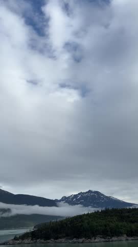 Clouds Over Mountains and Calm Fjord Water in Alaska

Low clouds and fog rolling over green mountains and calm fjord water in Alaska. Serene coastal landscape with forested hills and distant snow capped peaks. Perfect for nature, travel and background footage.