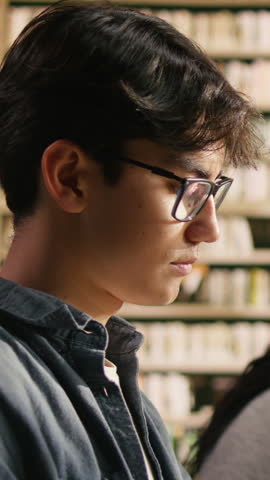Vertical composition: A young man reads open book at library study table, presenting shared study, mentoring and academic cooperation.