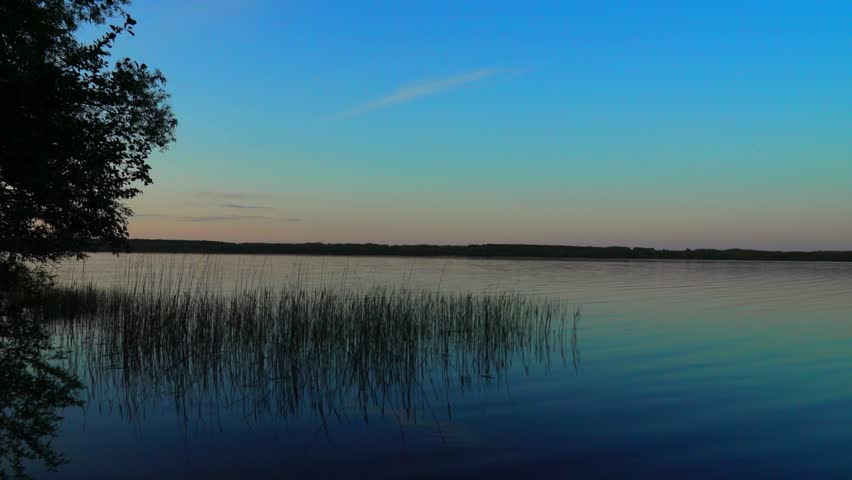 The sun begins to set over a large lake, casting soft light across the water