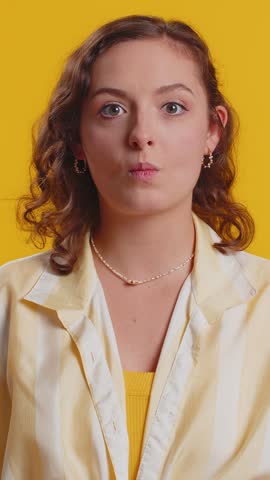 Surprised funny comical playful young woman making fish grimace pout lips, smooching choking, looking with shocked dumb idiotic expression, doing duck face, fooling around. Lady on yellow background