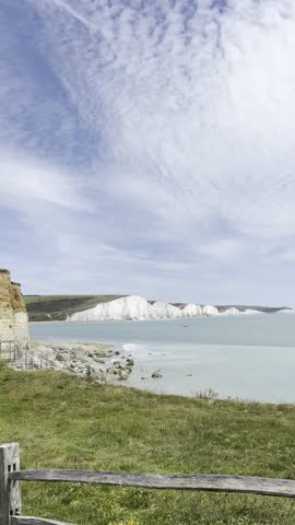 Panoramic view of the Seven Sisters chalk cliffs and calm coastal waters, framed by green clifftop grassland, East Sussex, England.