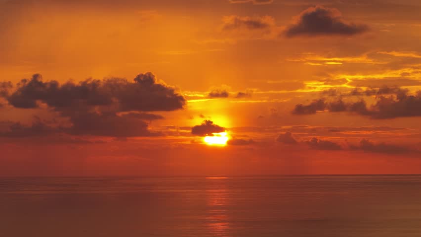Bright sun setting over the calm ocean with dramatic orange sky and moving clouds. Beautiful tropical scenic view from Uvita, Costa Rica