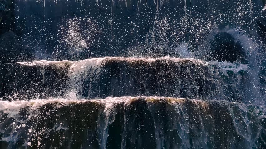 Close up of water cascading over stone steps of a decorative park waterfall in Istanbul, with bright splashes sparkling in sunlight - slowmo. Detailed droplets and flowing streams in slow motion