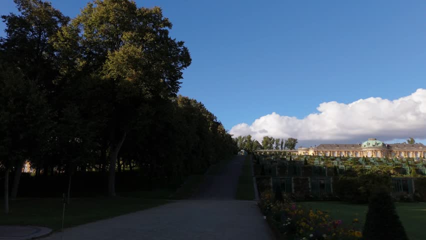 A gilded statue tops a stone column overlooking a manicured lawn with the New Palace visible in the distance at Sanssouci Park, Potsdam.