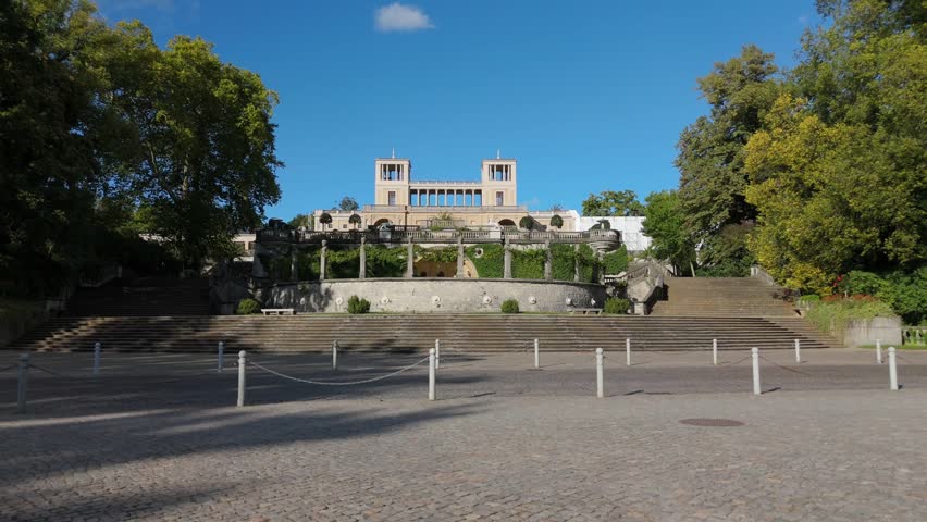 An empty cobblestone plaza stretches before the terraced Orangery Palace in Sanssouci Park, Potsdam.