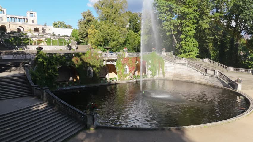 The ornamental fountain Springbrunnen and pond sit before a palace backdrop framed by trees in Sanssouci Park, Potsdam.