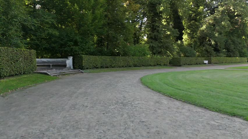 A curved gravel path winds between manicured hedges in a formal Potsdam park garden.