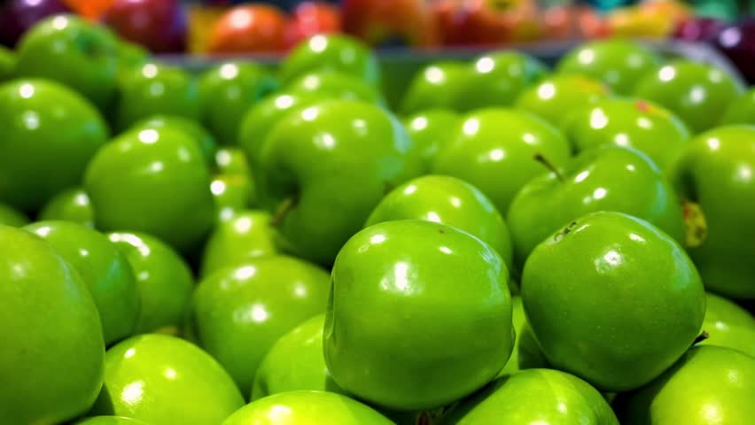 A refreshing and crisp close-up shot capturing a massive layout of shiny green Granny Smith apples at a grocery store produce section.
