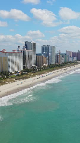 Vertical screen. Coastal view of Myrtle Beach, South Carolina, showcasing sandy beach, ocean waves, and high-rise buildings under a bright blue sky