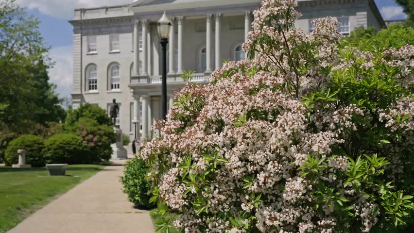 Cinematic dolly in and upward movement through colorful flowers revealing the historic New Hampshire State House in Concord New Hampshire on a beautiful summer day.