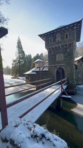 Charming stone gate tower and wooden bridge covered in winter snow by a frozen pond