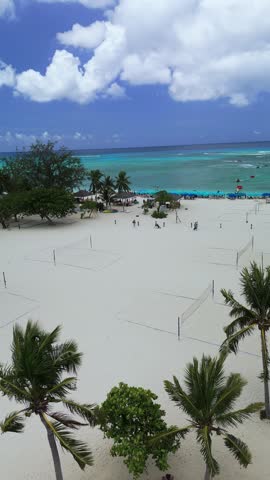 Aerial view of Grand Cayman beach with white sand, volleyball nets, palm trees, and turquoise water in Cayman Islands.