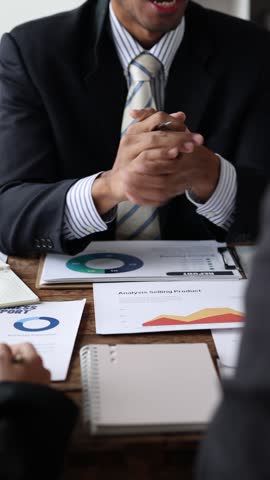 Professional business executives wearing suits negotiating financial strategy, shaking hands while analyzing charts and discussing investment details during collaborative corporate meeting.