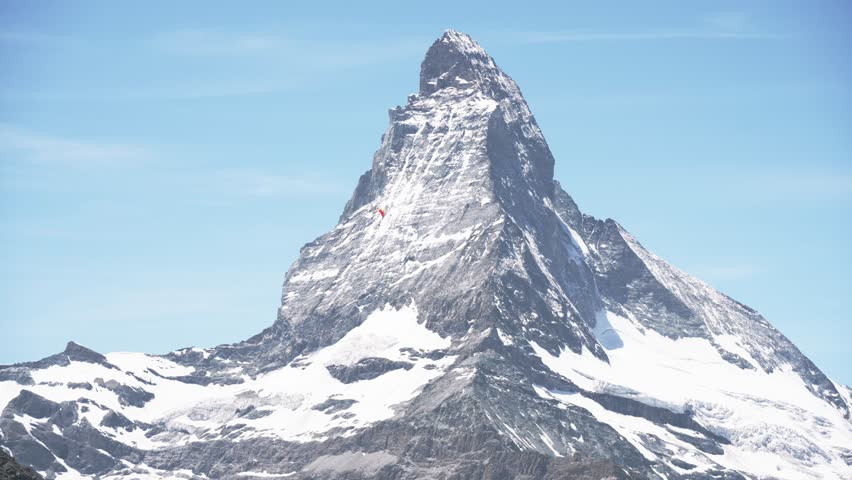 Red paraglider soaring across the majestic matterhorn on a clear summer day in the swiss alps