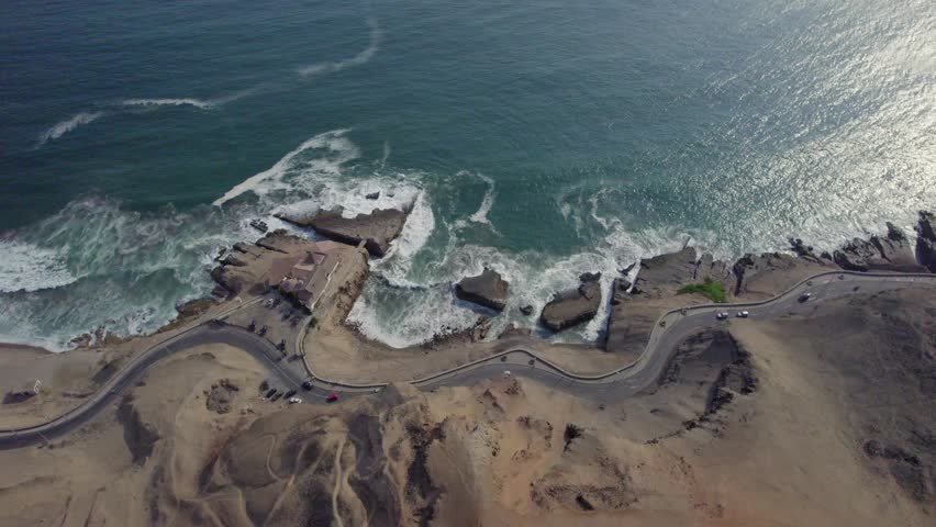 Aerial view of Morro Solar coastline with winding roads, rocky cliffs, and ocean waves in Chorrillos, Lima Province, Peru.