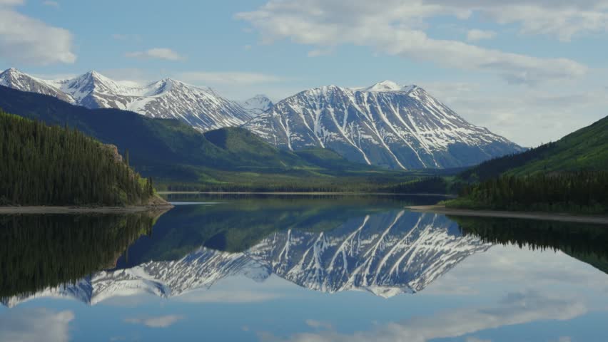Serene landscape reflecting snow capped mountains and evergreen forests on Tutshi Lake, Yukon