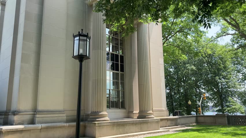 Architectural detail MIT campus in Cambridge, Massachusetts, showing a neoclassical building facade with tall fluted columns, a window bay, and a tree-lined riverside setting on a bright summer day.