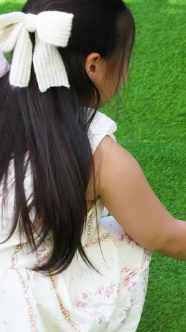 A young girl in a floral dress feeds a black rabbit from a small pan