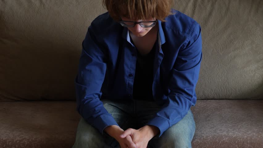 Young man (zoomer) with messy hair leaning forward
 and holding his head. Visibly troubled, feeling stress, burnout and mental exhaustion. Depression and mental health concept.