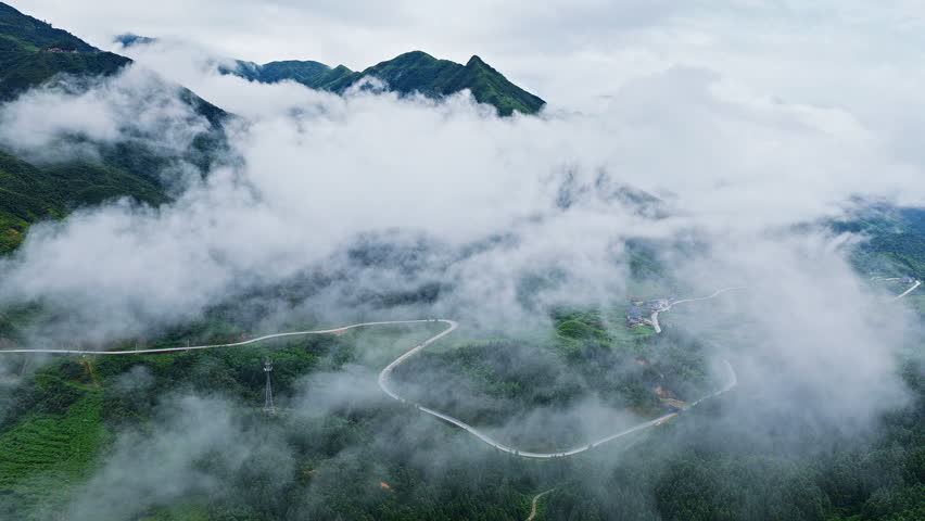 Aerial view of a winding road through misty green mountains under thick clouds in Guizhou, China