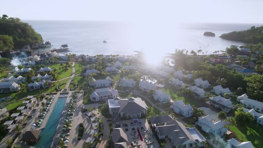 High-altitude aerial footage tracking downward over a luxury resort in Saint Vincent and the Grenadines. The shot reveals the layout of the property, including villa clusters and a long swimming pool