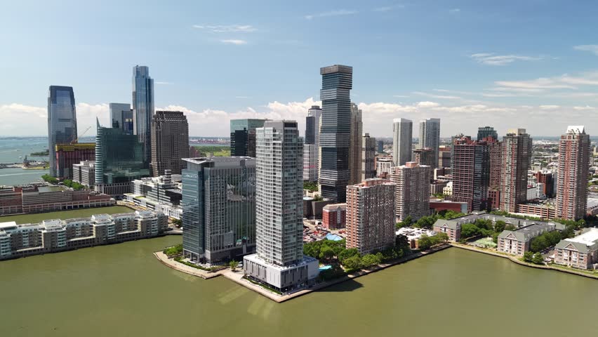 Spectacular aerial view of the jersey city skyline, featuring modern skyscrapers and residential buildings along the hudson river waterfront on a clear, sunny day with blue skies
