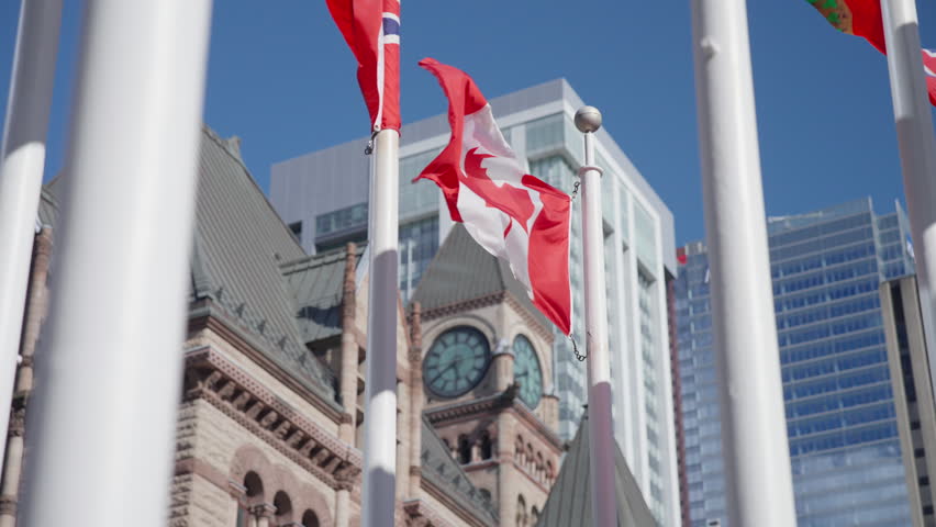 Canadian flag waves in the wind above the Old Toronto City Hall clock tower with modern downtown buildings in the background, Slow Motion