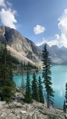 A vertical view of Moraine Lake with turquoise water framed by pine trees and the towering peaks of the Valley of the Ten Peaks in Canada