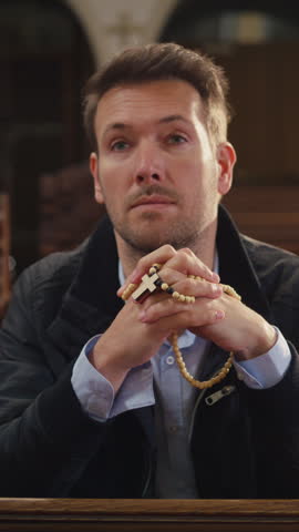 Private moment of prayer, a man sitting on a wooden pew in a peaceful, empty Christian church, praying with rosary beads.