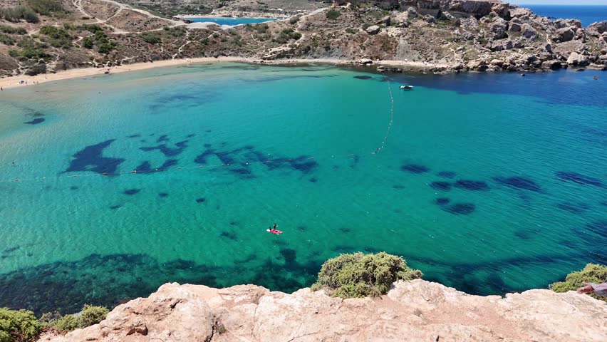 A 4k aerial view of Riviera Bay in Malta with clear water golden sand and visitors on a sunny day