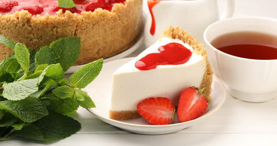 Piece of tasty cheesecake with strawberries and tea served on white wooden table, closeup. Camera moving left
