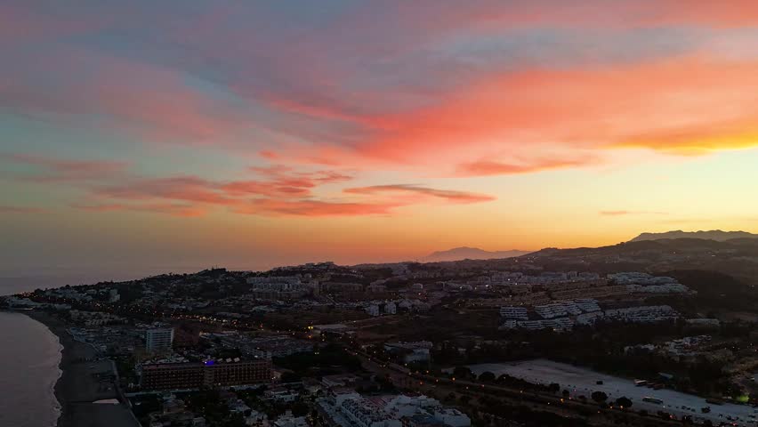 Hyperlapse aerial drone footage of a sunset over La Cala de Mijas, Costa del Sol, Spain, with pink and orange clouds, coastal town lights, and the Mediterranean sea