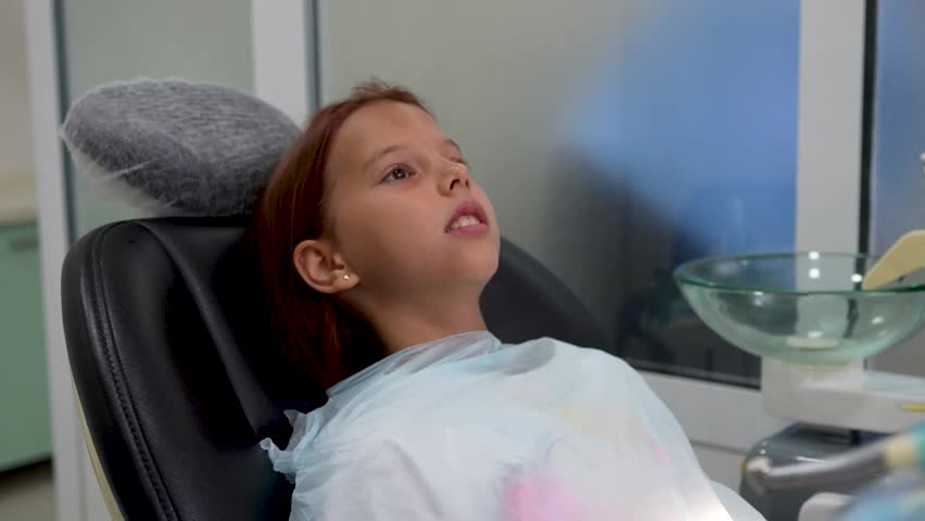 Little girl sitting in dental chair during treatment pause in clinic close up.