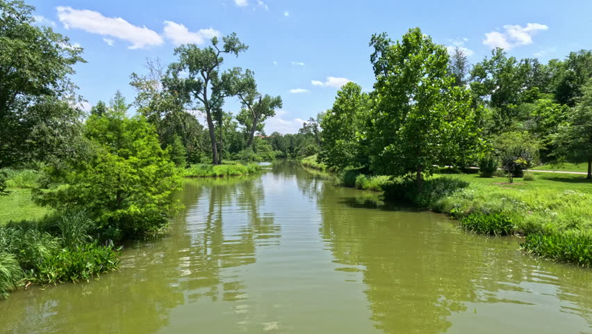 Gentle Water Ripples on Park River with Mature Trees. A peaceful static view capturing beautiful water ripples flowing gently down a scenic river surrounded by massive old-growth trees at Forest Park in St. Louis, Missouri, USA.